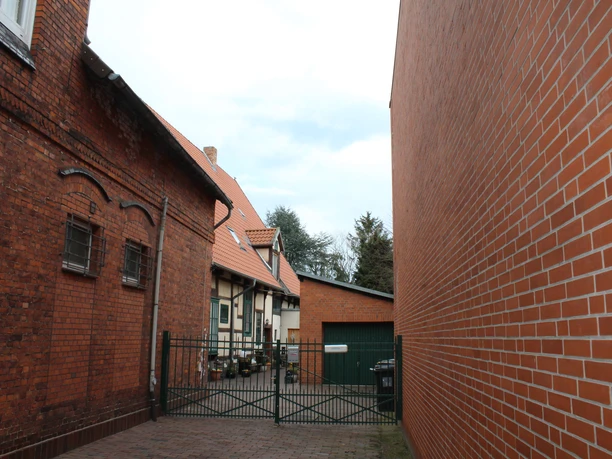 Brick building with red roof and gate to the courtyard, a tree on the left, a modern extension on the right.