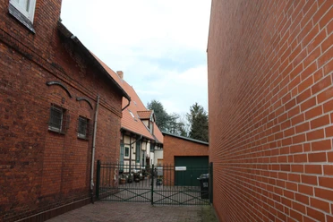 Beckmann Haus Bakstenen gebouw met rood dak en poort naar de binnenplaats, een boom aan de linkerkant, een moderne aanbouw aan de rechterkant.