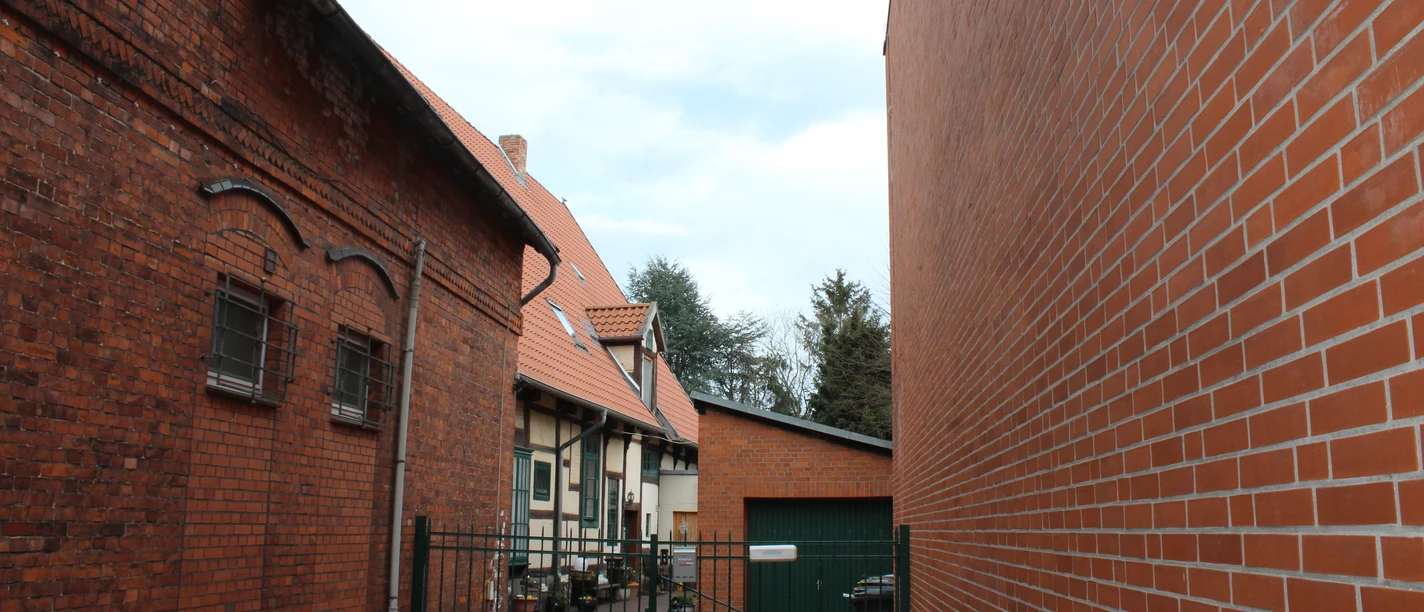 Beckmann Haus Brick building with red roof and gate to the courtyard, a tree on the left, a modern extension on the right.