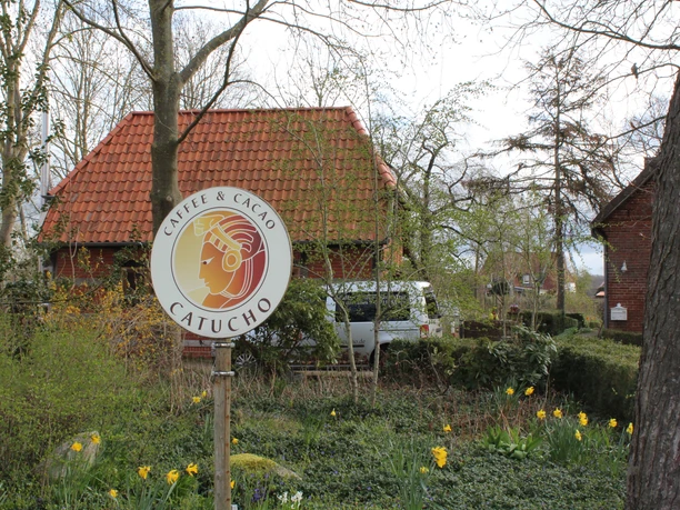 Café Catucho is set in a green garden with yellow flowers, trees and a red roof.