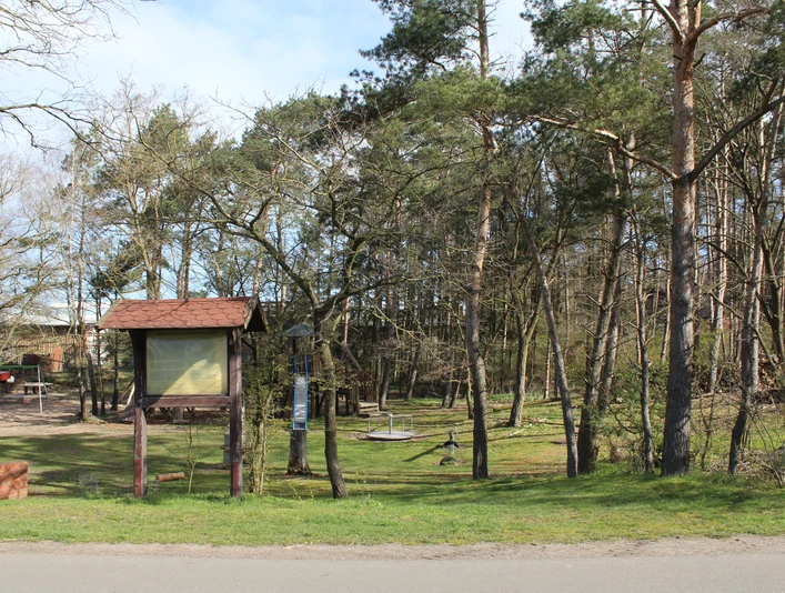 Beschilderter Eingangsbereich zu einem archäologischen Grabhügelfeld mit umliegenden Bäumen und Wald.
