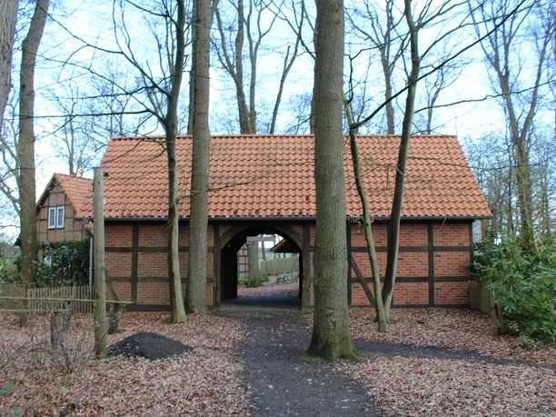 A half-timbered building with a red-tiled roof, surrounded by bare trees and a path covered with autumn leaves.