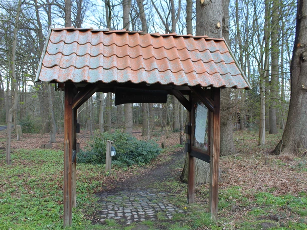 Freilichtbühne Holtebüttel: Eingang mit schindelbedecktem Torbogen, umgeben von Bäumen im Frühjahr.