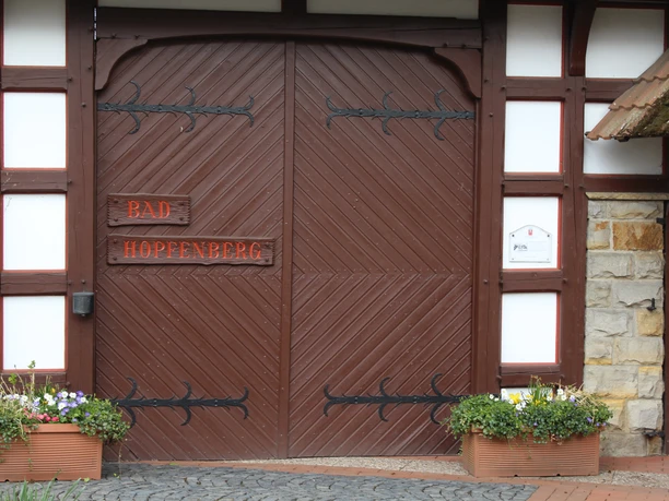 Bad Hopfenberg Historisches Holztor mit Aufschrift "Bad Hopfenberg", flankiert von Blumenkästen und Mauerwerk.