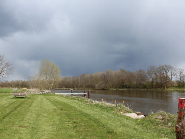 Schiffsanleger Heisterholz Grüner Rasen erstreckt sich zum Flussufer; im Hintergrund ruht ein wolkenverhangener Himmel.