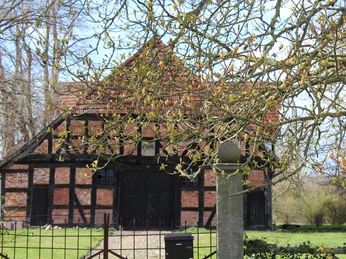 Behrenhof Historisches Fachwerkgebäude bei bewölktem Himmel, umgeben von blühenden Bäumen und grünem Rasen.