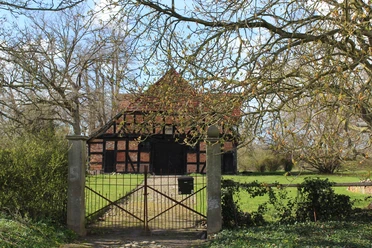 Behrenhof Fachwerkhaus mit Backsteinmauern hinter einem schmiedeeisernen Tor, umgeben von grüner Landschaft.