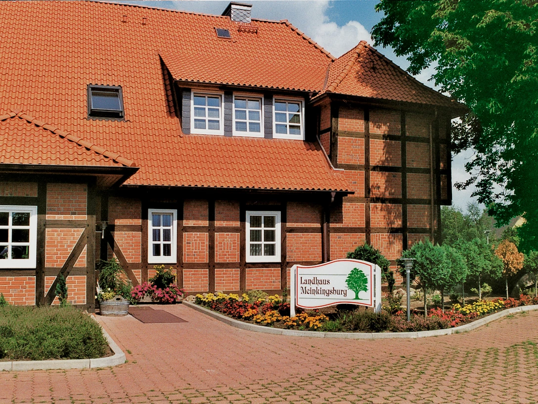 Hotel Landhaus Meinkingsburg Fachwerkhaus mit roten Ziegeln und blühenden Gärten; Hotelschild vorne; ländliche Umgebung.