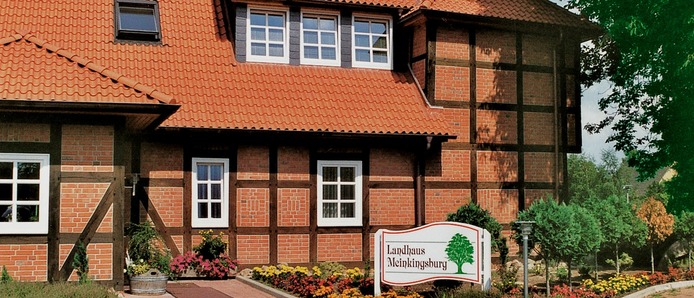 Hotel Landhaus Meinkingsburg Fachwerkhaus mit roten Ziegeln und blühenden Gärten; Hotelschild vorne; ländliche Umgebung.