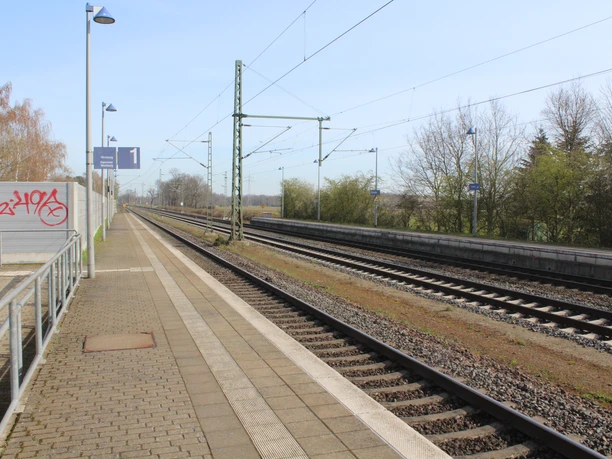 Bahnhof Dörverden mit leeren Gleisen, umgeben von Bahnschildern und kahlen Bäumen, sonniger Himmel.