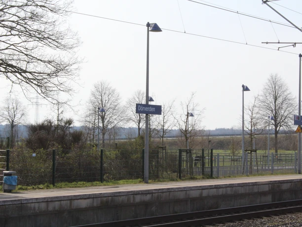 Bahnhof Dörverden Bahnhofsplattform in Dörverden mit Gleisen, umliegender Natur und Bahnhofsschildern bei klarem Wetter.