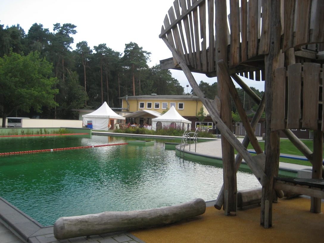 Restaurant am Waldbad Ein Restaurant mit gelber Fassade am Waldbad, umgeben von Bäumen, mit Blick auf das Schwimmbecken.