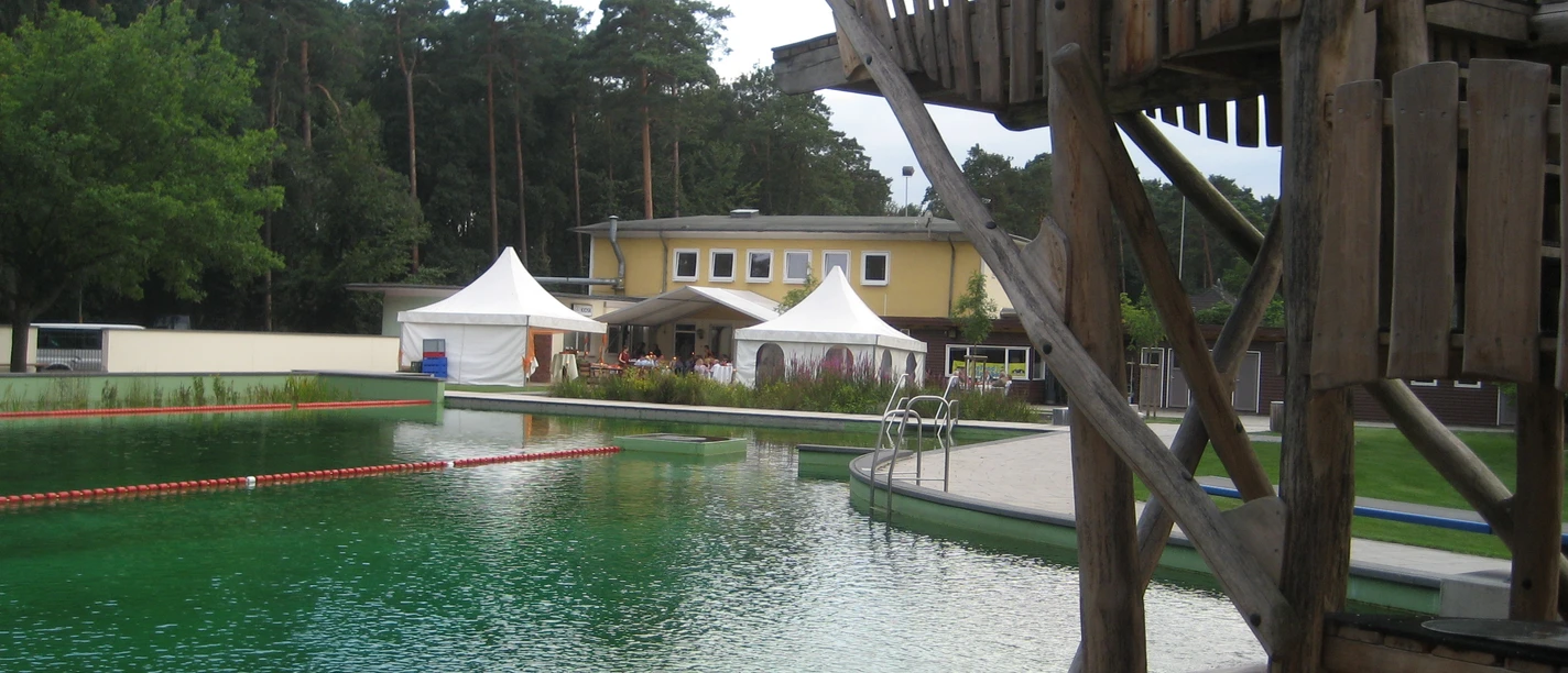 Restaurant am Waldbad Ein Restaurant mit gelber Fassade am Waldbad, umgeben von Bäumen, mit Blick auf das Schwimmbecken.