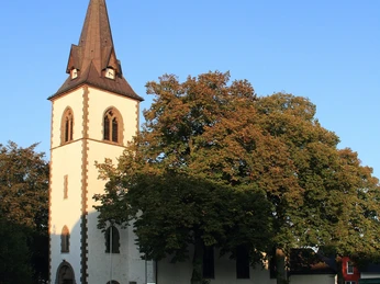 Kirche Tietelsen Weiße Kirche Tietelsen mit hohem Turm, umgeben von Bäumen und bei klarem, blauem Himmel.