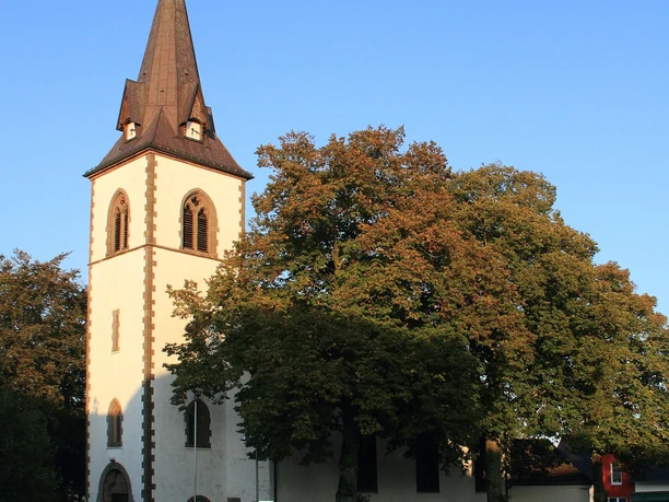 Kirche Tietelsen Weiße Kirche Tietelsen mit hohem Turm, umgeben von Bäumen und bei klarem, blauem Himmel.