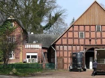 Historischer Gutshof mit zwei roten Backsteingebäuden, Pferdeanhänger und Pferd im Vordergrund.