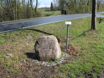 Gedenkstein Mariechen Lehmkuhl am Wegesrand mit Straßen- und Landschaftskulisse im Hintergrund.