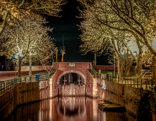 Siel in Greetsiel Historisches Sieltor in Greetsiel bei Nacht, beleuchtet von warmem Licht, umgeben von kahlen Bäumen.