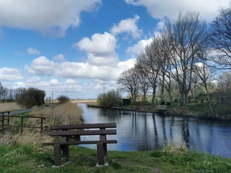 Broklandsau Bank an ruhigem Fluss mit Bäumen und weitem Himmel