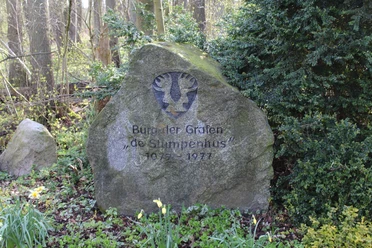 Gedenkstein aus Stein mit Inschrift "Burgen der Grafen de Stumpenhus 1975 - 1977" in einer grünen Waldszene.