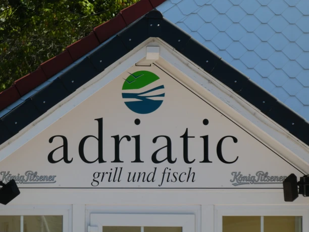 Restaurant "adriatic" sign with blue logo and lettering "grill und fisch" under a striking roof.