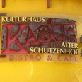 Gastro im KASCH Rostiges Metallschild mit der Aufschrift "Kulturhaus KASCH Alter Schützenhof Bistro & Café" an gelber Wand.Rusty metal sign with the inscription "Kulturhaus KASCH Alter Schützenhof Bistro & Café" on a yellow wall.Rustent metalskilt med påskriften "Kulturhaus KASCH Alter Schützenhof Bistro & Café" på en gul væg.Roestig metalen bord met het opschrift "Kulturhaus KASCH Alter Schützenhof Bistro & Café" op een gele muur.