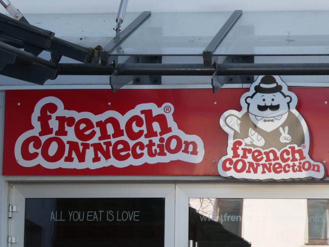 French Connection Eingangsbereich eines Restaurants mit dem Namen "French Connection" und einem Cartoon-Koch als Logo.Entrance area of a restaurant with the name "French Connection" and a cartoon chef as logo.Indgangsparti til en restaurant med navnet "French Connection" og en tegnet kok som logo.Entree van een restaurant met de naam "French Connection" en een cartoonkok als logo.