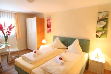 Landhotel Bergischer Hof Helles Doppelzimmer mit zwei Einzelbetten, dekorativen Bildern, Schrank und Tisch mit Stühlen.
