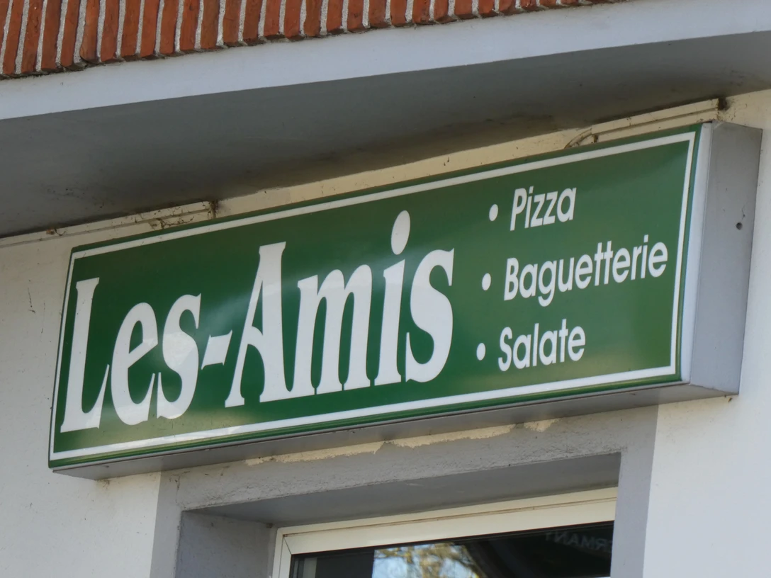 Grünes Schild von "Les Amis" mit den Angeboten Pizza, Baguetterie und Salate, auf Backsteinwand.Green sign from "Les Amis" with the offers pizza, baguetterie and salads, on a brick wall.Grønt skilt fra "Les Amis" med tilbud om pizza, baguetterie og salater på en murstensvæg.Groen bord van "Les Amis" met de aanbiedingen pizza, baguetterie en salades, op een bakstenen muur.