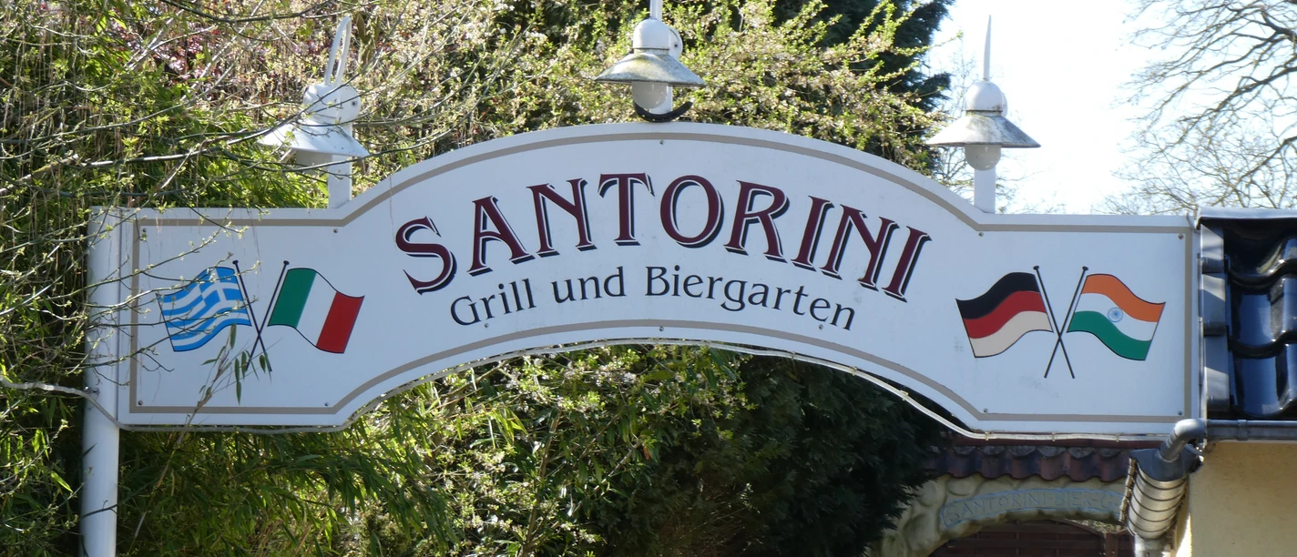 The entrance sign of the Santorini restaurant shows a Greek and German flag with green surroundings.