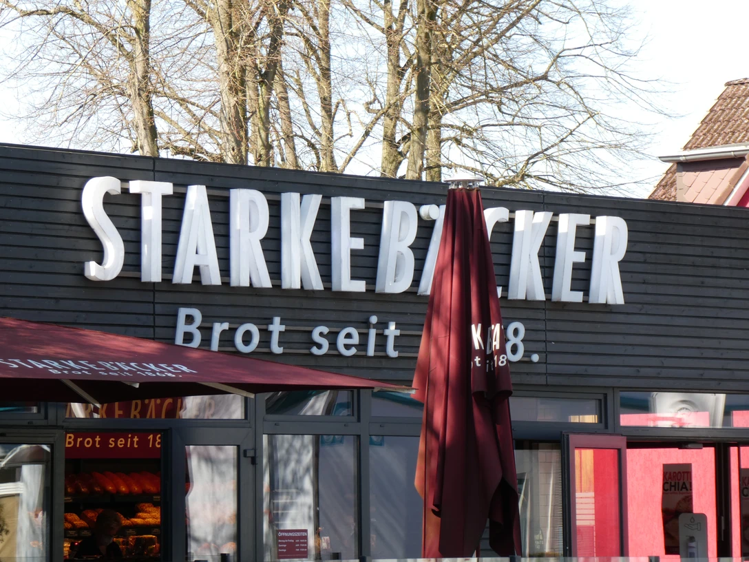Starke Bäcker Ein Bäckereigebäude mit Holzfassade und großer Beschriftung "Starke Bäcker" sowie textilbespannten Markisen.