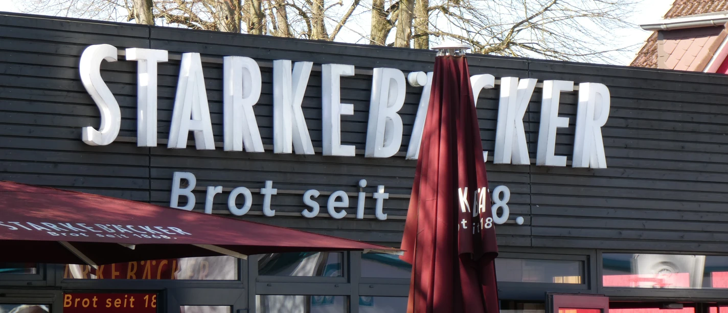 Starke Bäcker Ein Bäckereigebäude mit Holzfassade und großer Beschriftung "Starke Bäcker" sowie textilbespannten Markisen.