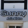 Sunny Asia Bistro Leuchtendes Schild mit der Aufschrift "Sunny Asia Bistro" an einer Gebäudefassade mit Fachwerkelementen.
