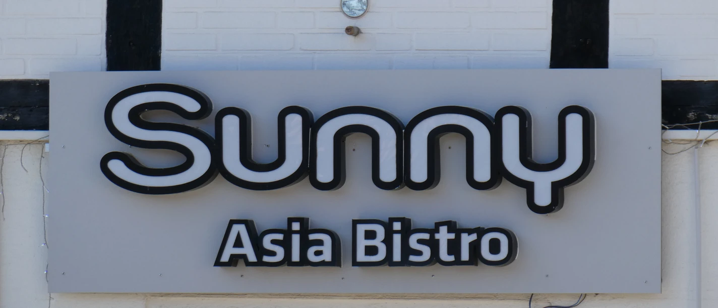 Sunny Asia Bistro Leuchtendes Schild mit der Aufschrift "Sunny Asia Bistro" an einer Gebäudefassade mit Fachwerkelementen.