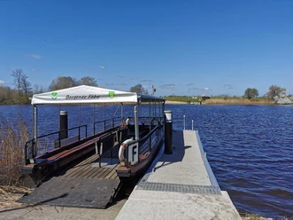 Bargener Fähre Kleine Fähre am Steg vor breitem Flussufer