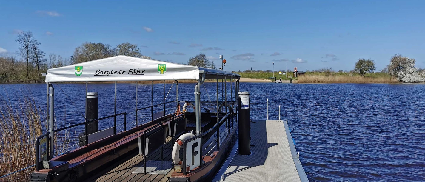Bargener Fähre Kleine Fähre am Steg vor breitem Flussufer