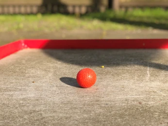 Minigolf Ein leuchtend roter Minigolfball liegt auf einer Betonbahn, umrahmt von einem roten Begrenzungsrand.
