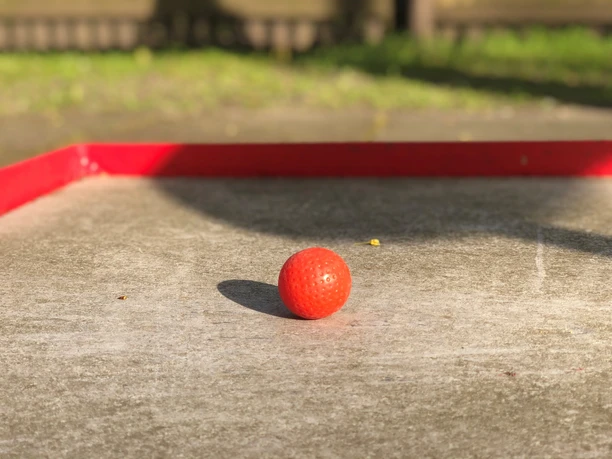 Minigolf Ein leuchtend roter Minigolfball liegt auf einer Betonbahn, umrahmt von einem roten Begrenzungsrand.