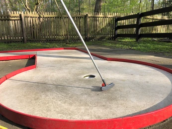 Ein Minigolfplatz mit einer roten Umrandung und einem Putter, der auf einer kreisförmigen Bahn liegt.