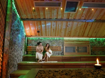 H2O Sport- und Freizeitbad Herford-Eventsauna Vaikutus Zwei Personen sitzen in einer modernen Sauna mit Holzbänken und Steinwänden, atmosphärisch beleuchtet.