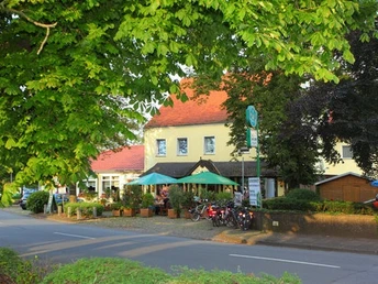 Hotel und Restaurant mit gelber Fassade, grüner Terrasse und Fahrrädern daneben, umgeben von Bäumen.