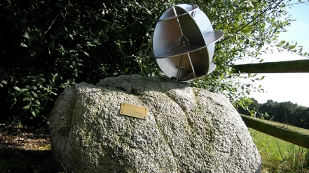 NRW Nordpunkt Metallskulptur auf großem Stein, umgeben von Grün, mit kleinem Messingschild auf sonniger Wiese.