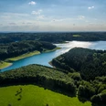 Große Dhünn- Talsperre Panoramablick auf eine weitläufige Landschaft mit Seen, Wäldern und grünen Wiesen unter blauem Himmel.