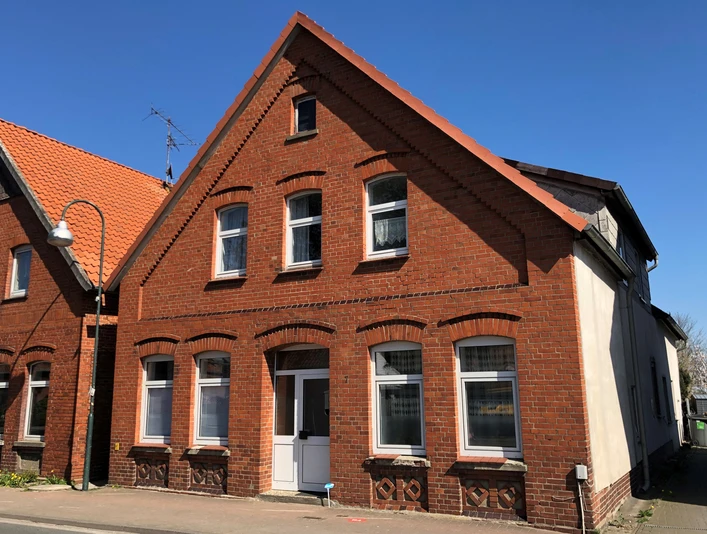 Ehem. Synagoge Rehburg Backsteingebäude mit weißen Fenstern, spitzem Dach und Eingang auf einer ruhigen Straße unter blauem Himmel.