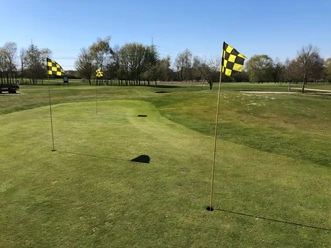 Uitzicht op een goed onderhouden, uitgestrekte golfbaan met vlaggen, omringd door bomen en blauwe lucht.
