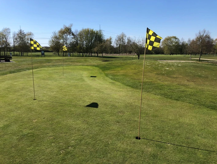 Golfplatz Rehburg-Loccum Aussicht auf einen gepflegten, weitläufigen Golfplatz mit Fahnen, umgeben von Bäumen und blauem Himmel.