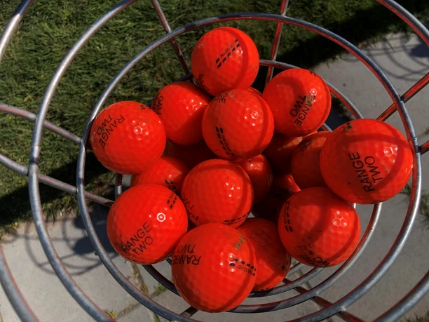 Golfbälle A close-up of red golf balls in a metal basket on green grass in sunny weather.