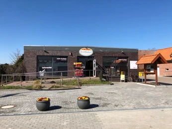 Moderner Dorfladen in Leeser aus rotem Backstein mit barrierefreiem Zugang und bepflanzten Vasen.