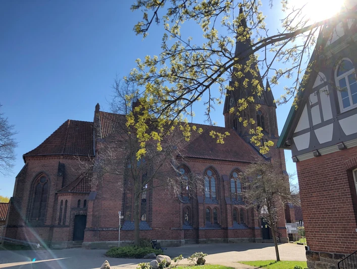 Kirche Leese Backsteinkirche mit hohem Turm und Spitzbogenfenstern, umrahmt von Bäumen unter klarem, blauen Himmel.
