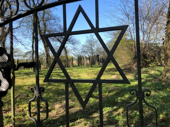Schwarz metallene Torverzierung mit Davidstern blickt auf grünen jüdischen Friedhof unter blauem Himmel.